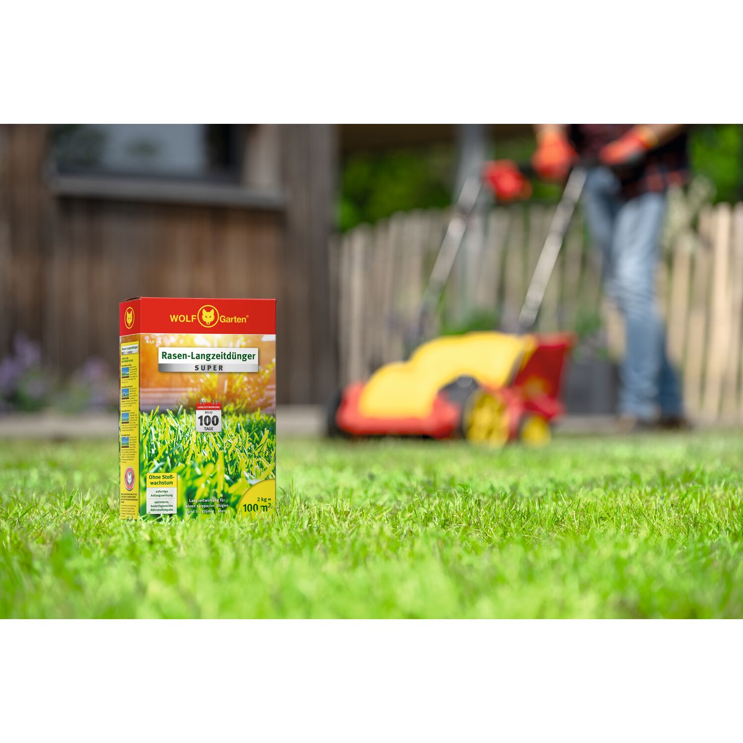 WOLF-Garten Long-Term Lawn Fertilizer "Super"" R-LD 100 folding box standing on a lawn with lawn mowing activities in the background"