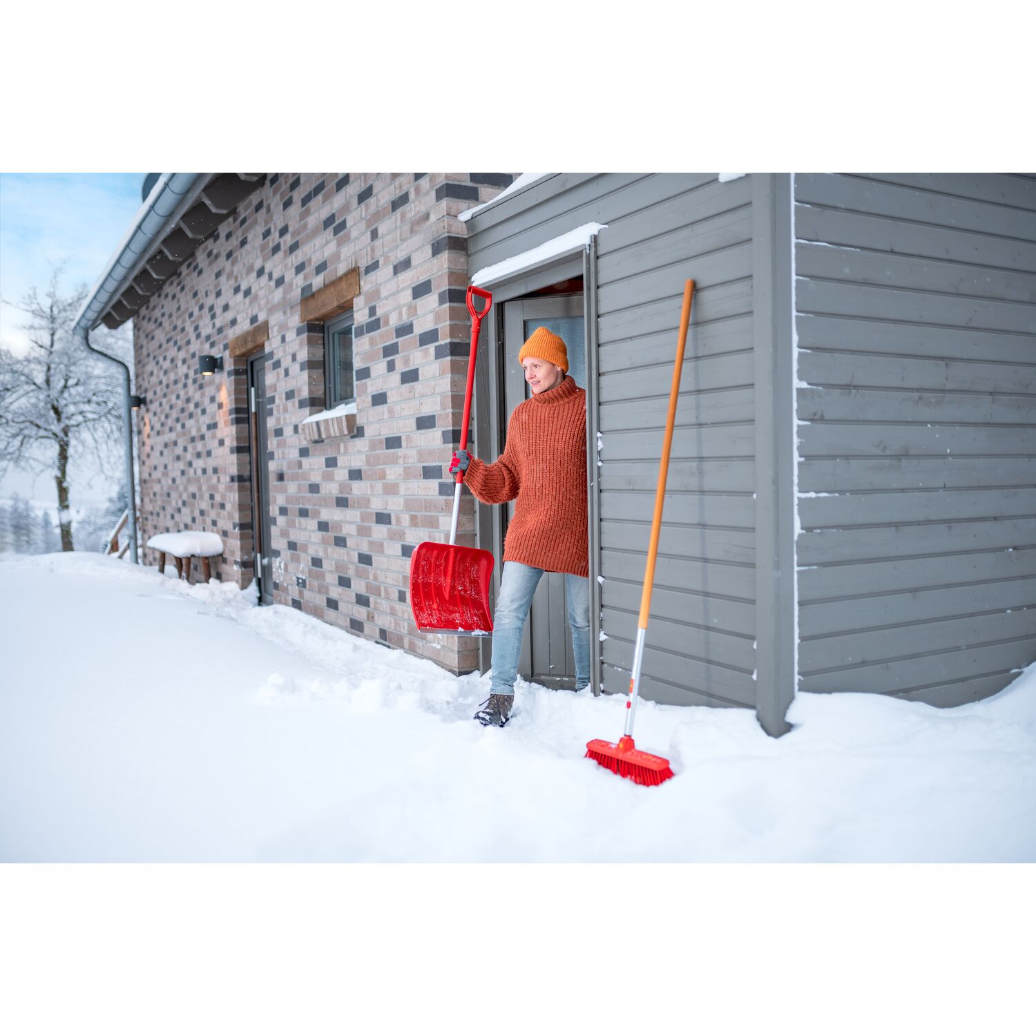 A woman steps out of the shed with the SN-M 42 / ZM-AD 120 snow shovel from WOLF-Garten in hand